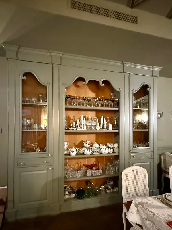 A grey-green cabinet full of old china and crystal
